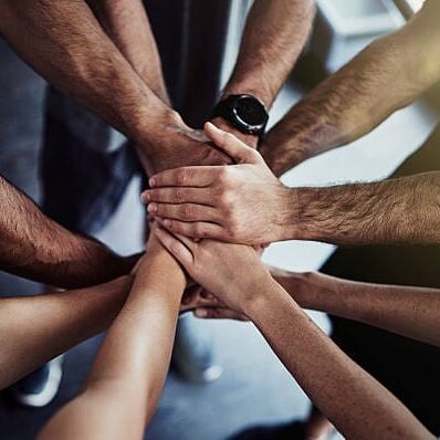 Cropped shot of a group of fit people joining their hands in unity at the gym